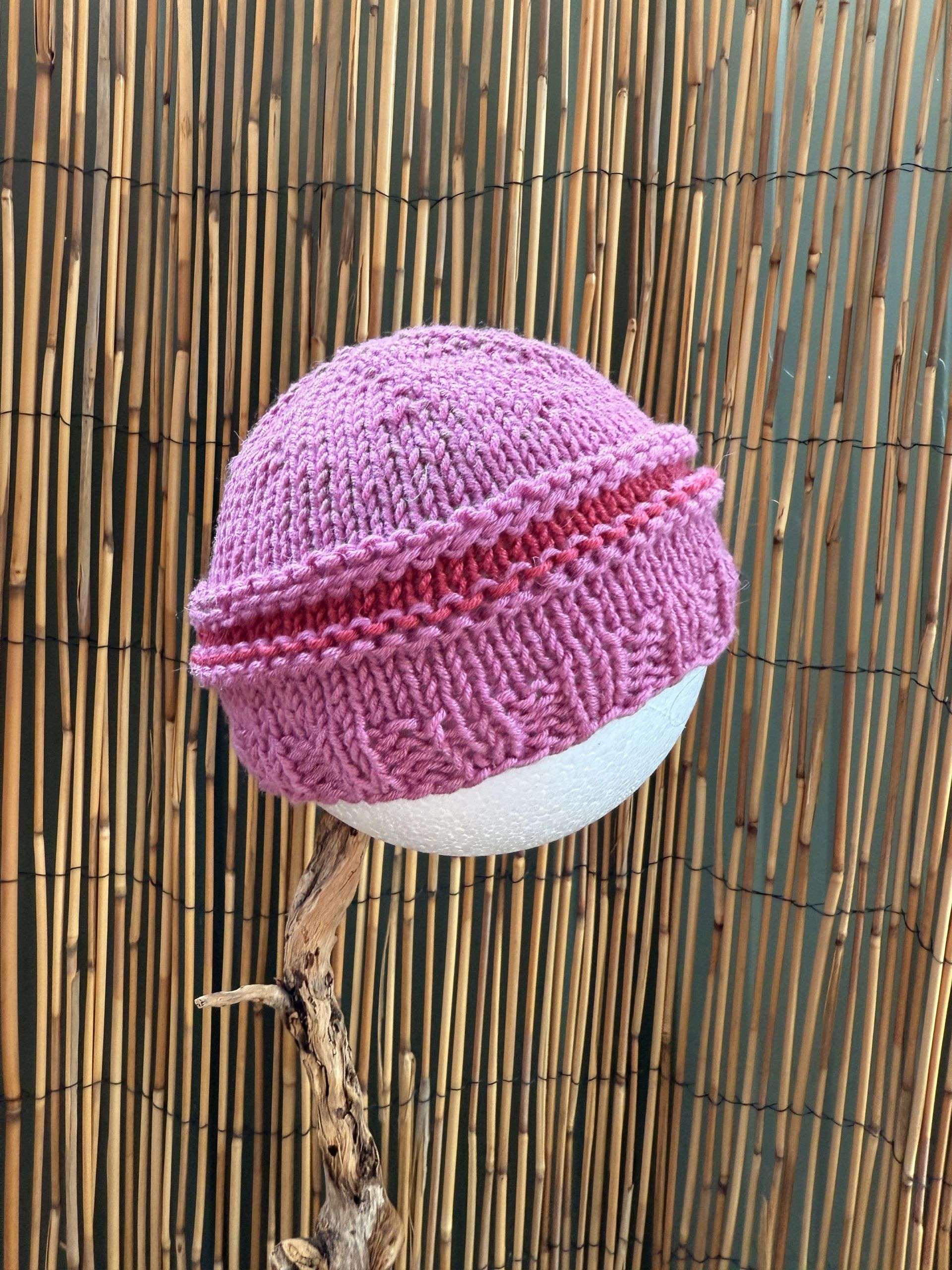 A soft pink baby beanie handmade with a cheeky coral stripe, sized for the smallest heads.
