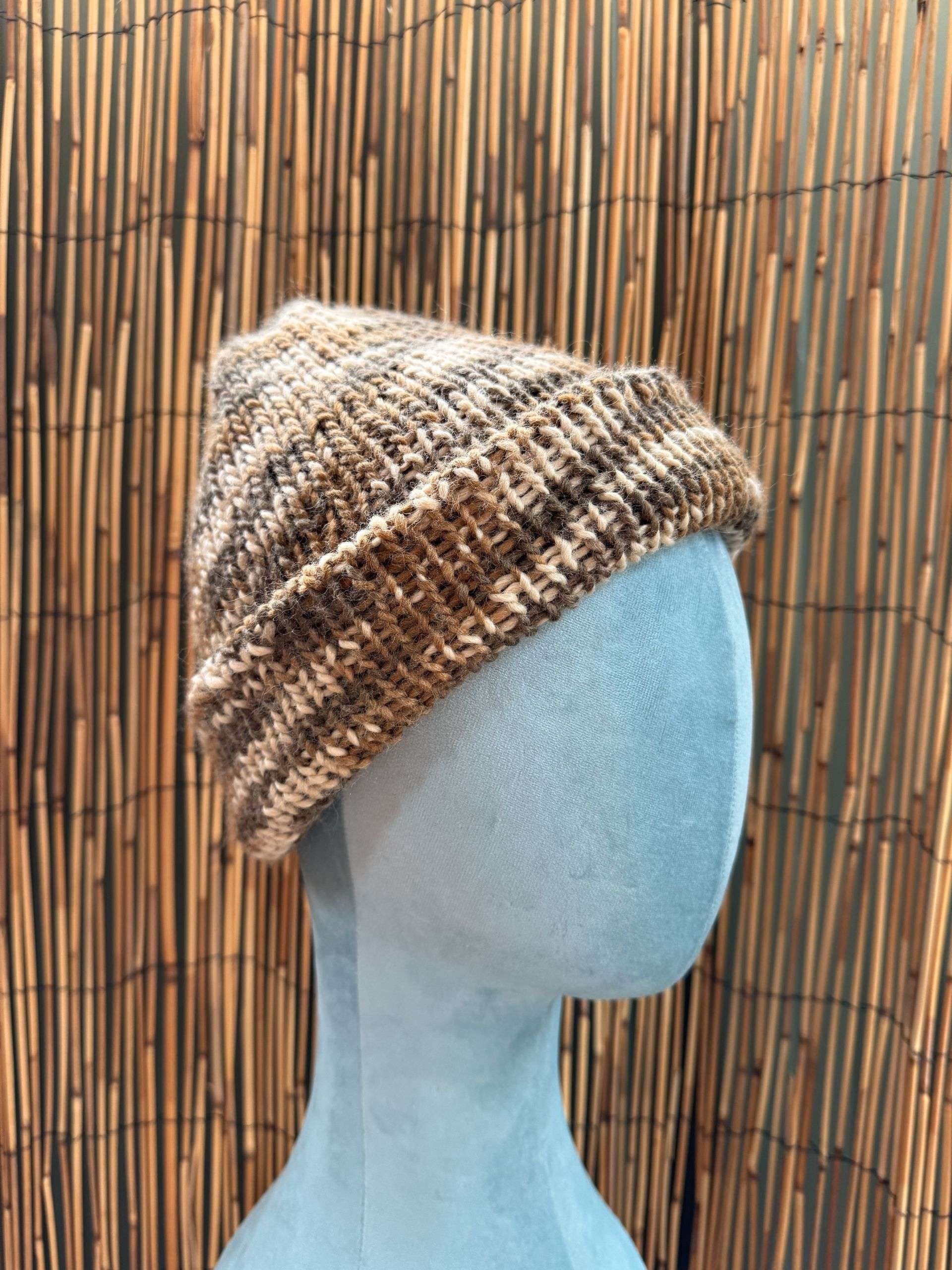A cosy brown and cream marl adult beanie, handknitted with the kind of texture that begs to be touched.