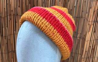 A striking striped adult beanie in gold and red, handmade knitwear with a cheerful glow.