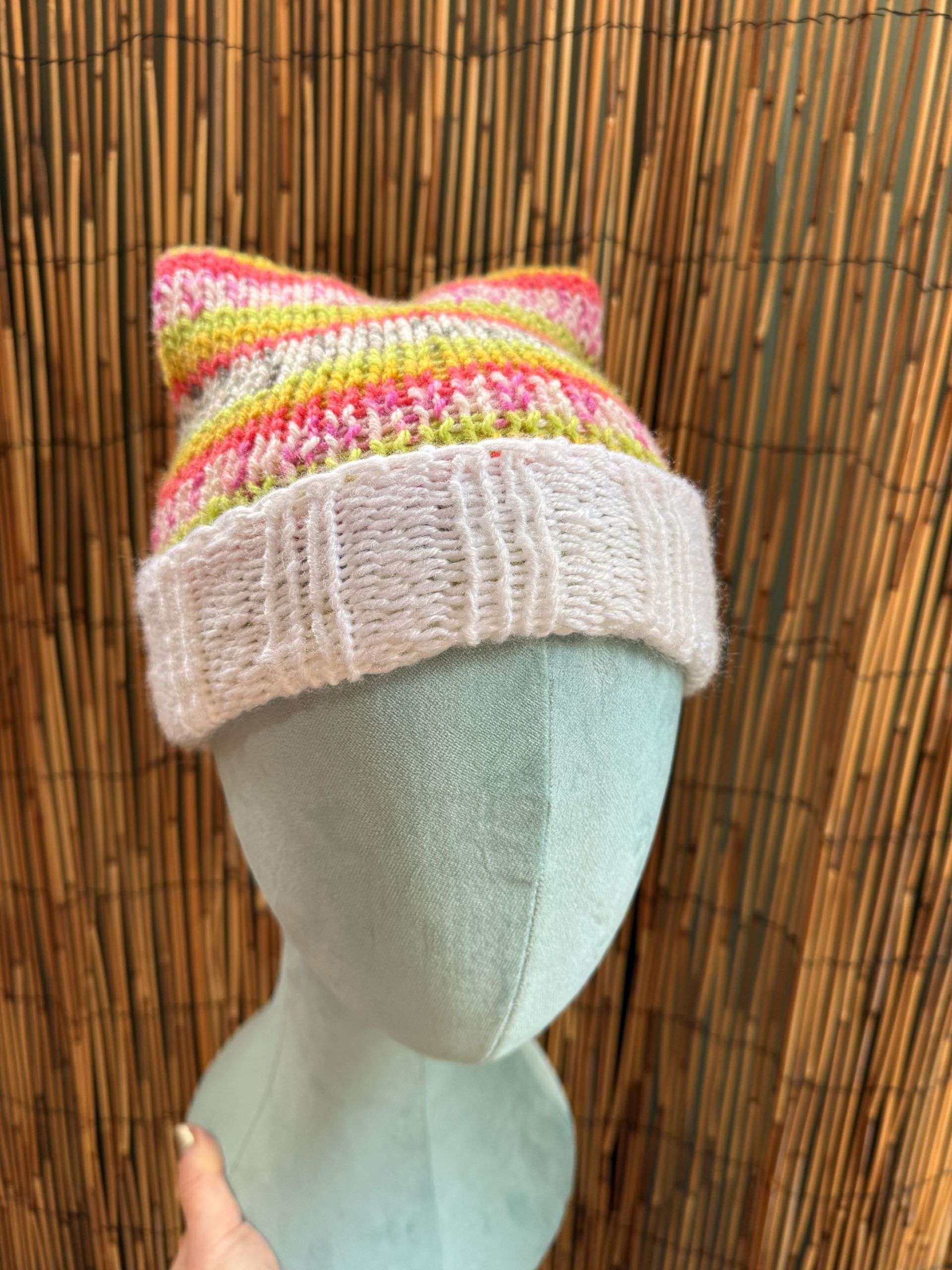 Two perky ears and a rainbow of pink and yellow stripes, this cat ear beanie is handknitted pure whimsy.